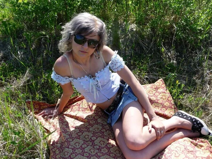 Gray-haired beauty posing naked outdoors on a blanket