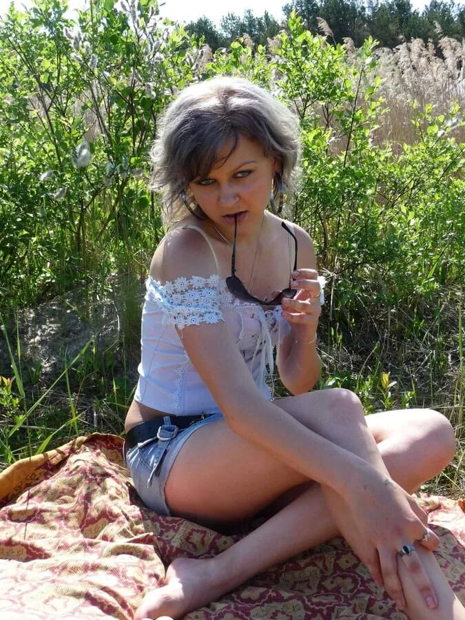 Gray-haired beauty posing naked outdoors on a blanket