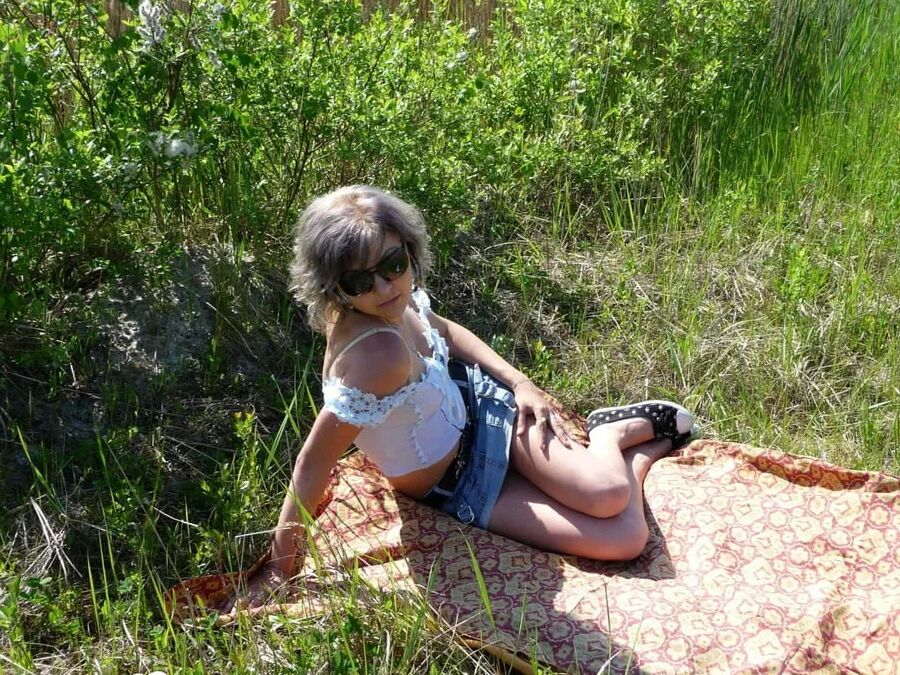 Gray-haired beauty posing naked outdoors on a blanket