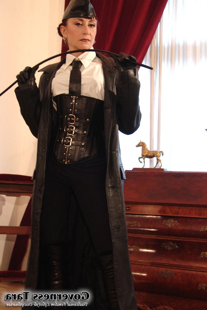 20P Twisted corsetted domina poses in spike heel leather boots