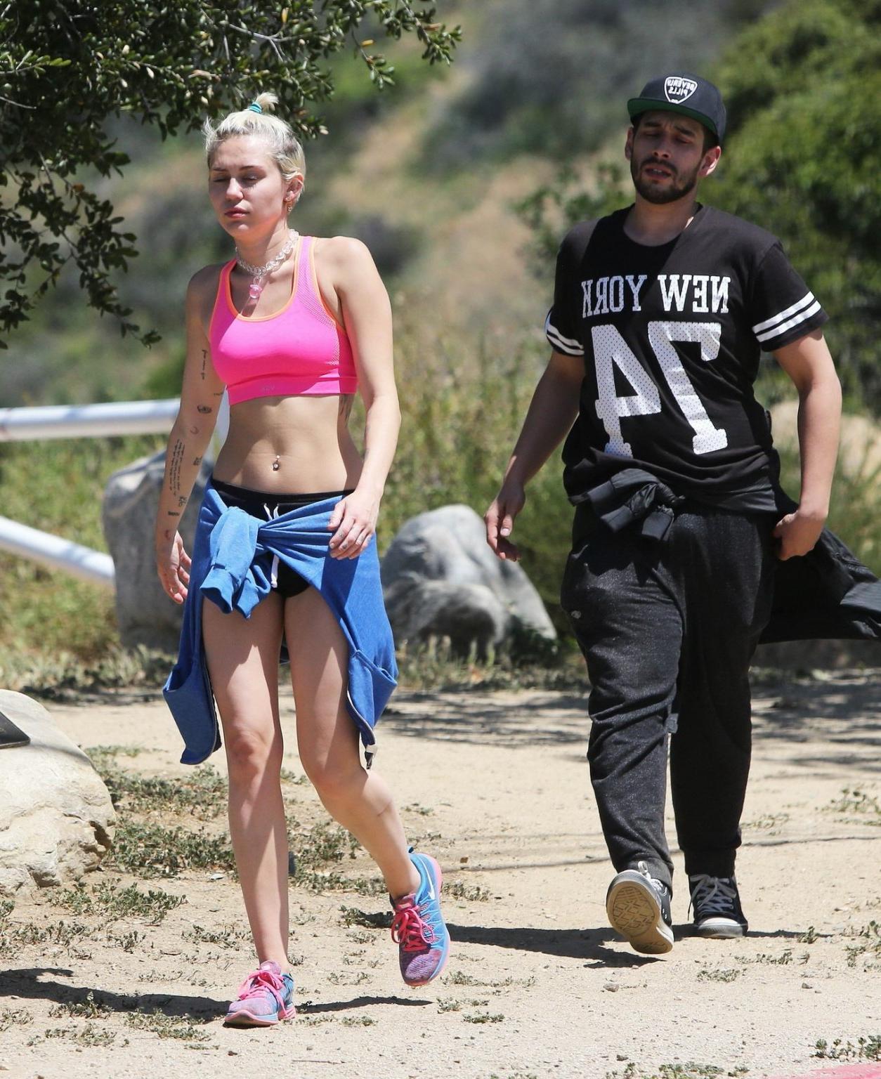 16P Miley Cyrus wearing pink sports bra and shorts out for a hike in LA