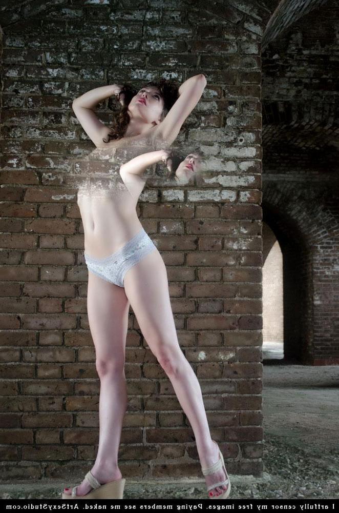 16P Brunette model Blush strips and teases in a brick wall basement