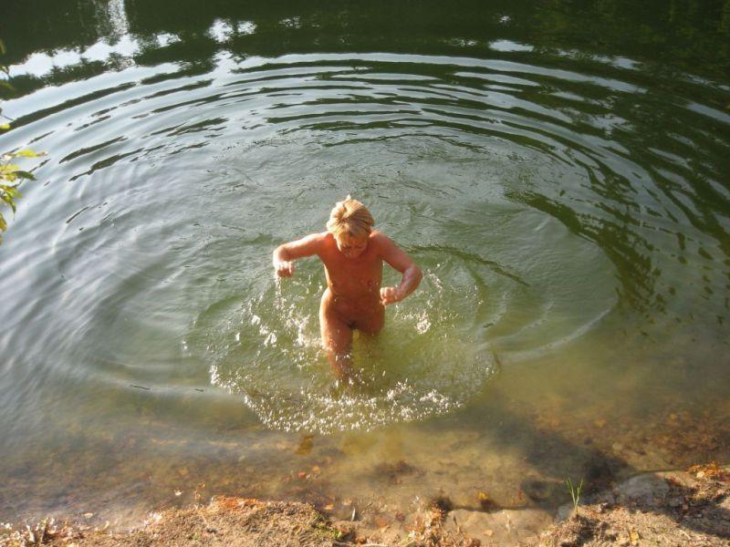 15P Brunette nudist kicks up some water at a nude beach