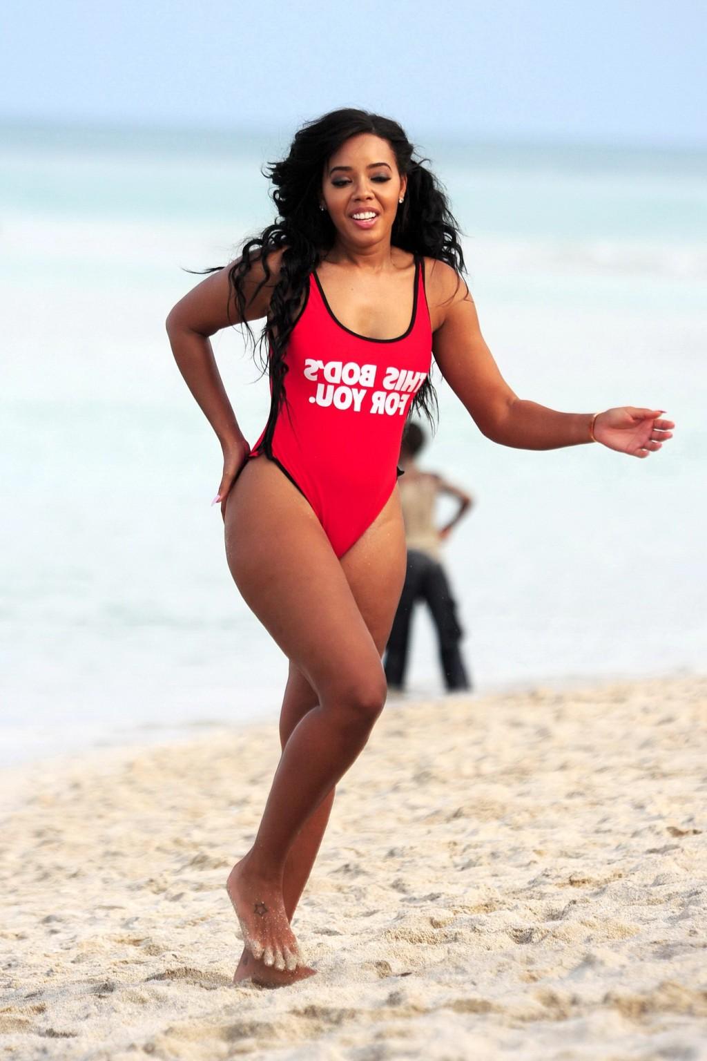 12P Angela Simmons in red swimsuit doing a bridge on a beach in Miami