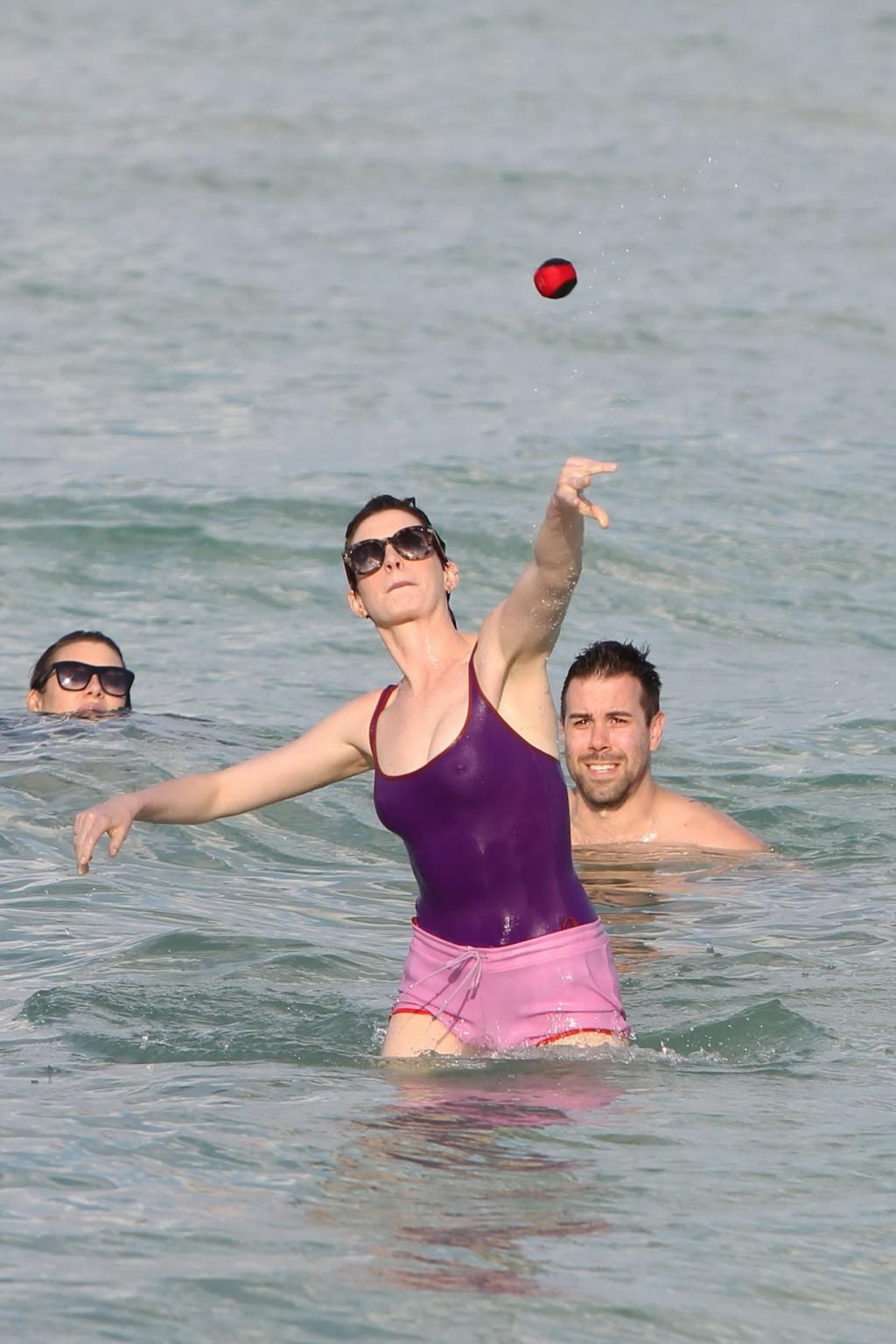 16P Anne Hathaway wearing wet purple see-through swimsuit and shorts at the beach in