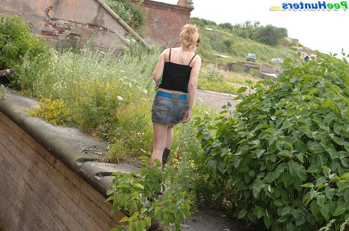 16P Cute young blondie makes water behind a lush shrub