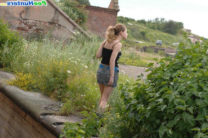 16P Cute young blondie makes water behind a lush shrub