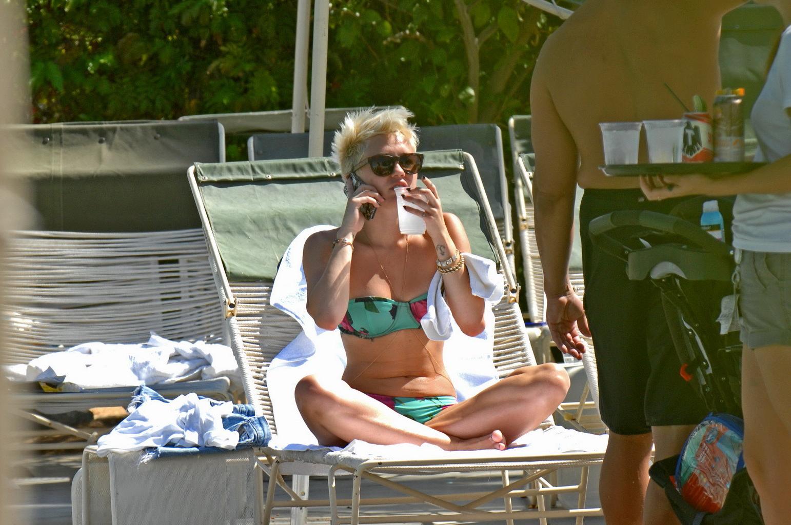 16P Miley Cyrus wearing floral tube bikini poolside at Palm Desert Hotel in Palm Spr