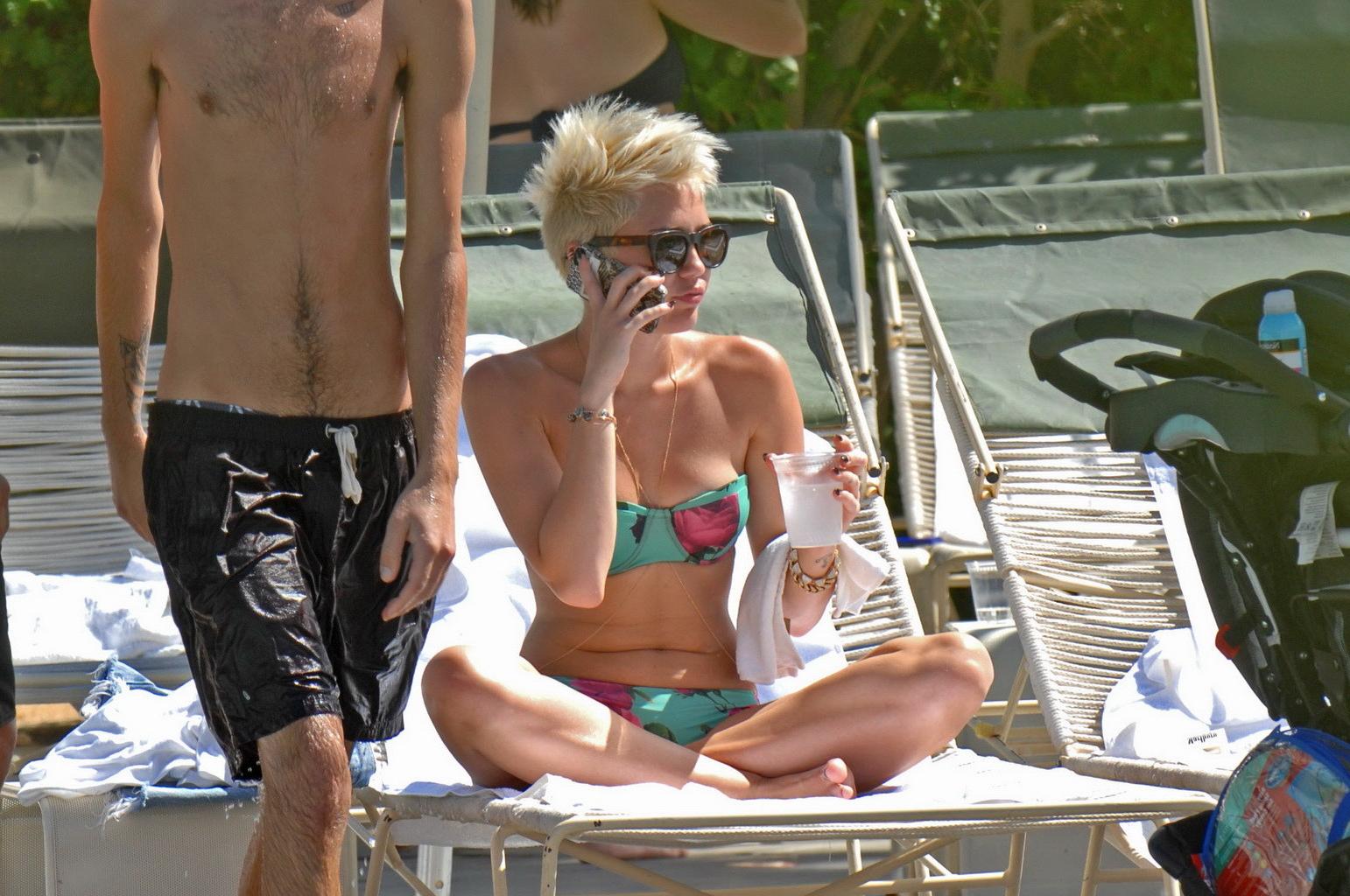 16P Miley Cyrus wearing floral tube bikini poolside at Palm Desert Hotel in Palm Spr