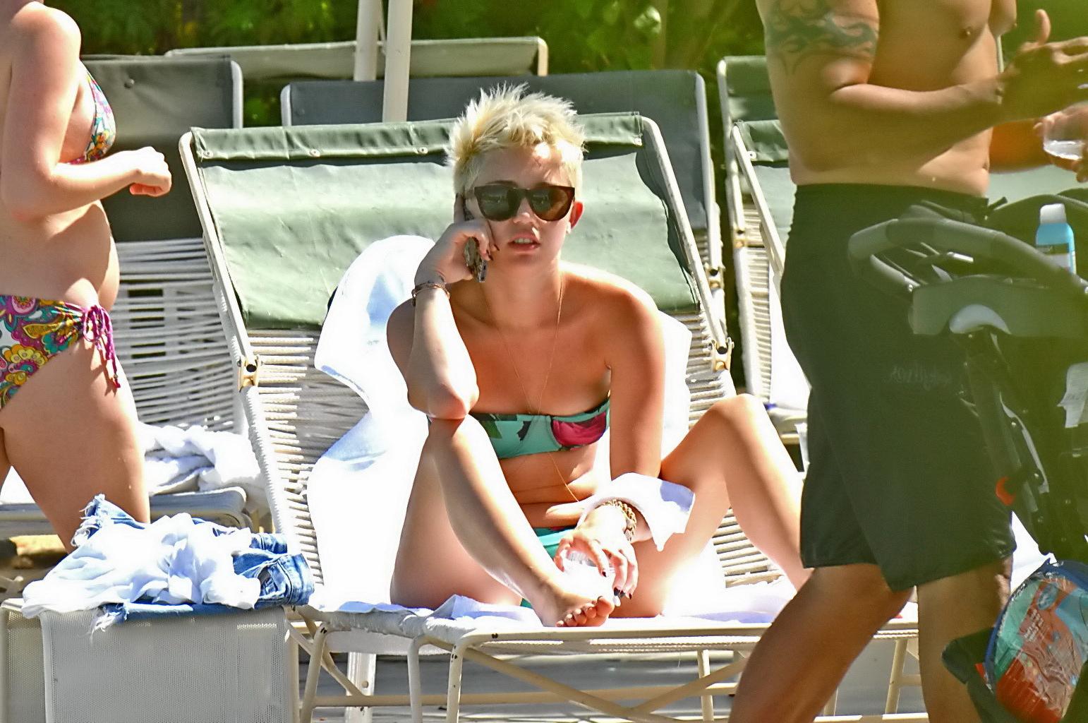 16P Miley Cyrus wearing floral tube bikini poolside at Palm Desert Hotel in Palm Spr
