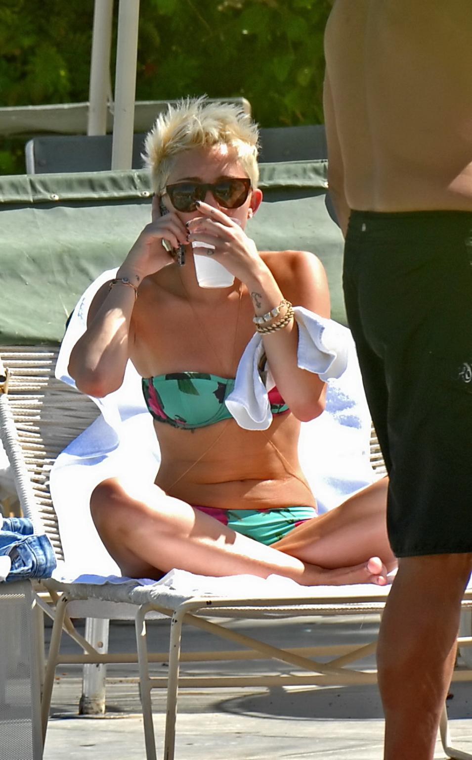 16P Miley Cyrus wearing floral tube bikini poolside at Palm Desert Hotel in Palm Spr