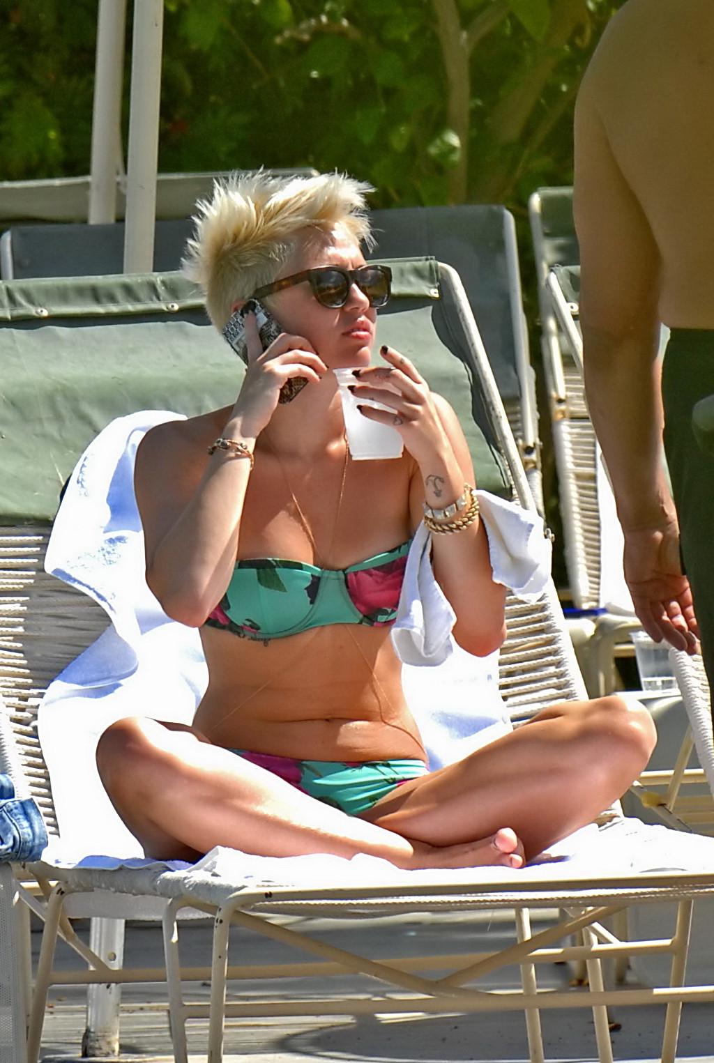 16P Miley Cyrus wearing floral tube bikini poolside at Palm Desert Hotel in Palm Spr