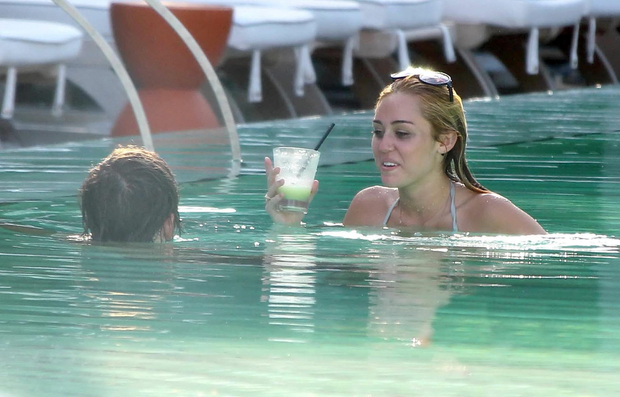 10P Miley Cyrus wearing white bikini at a hotel pool in Miami
