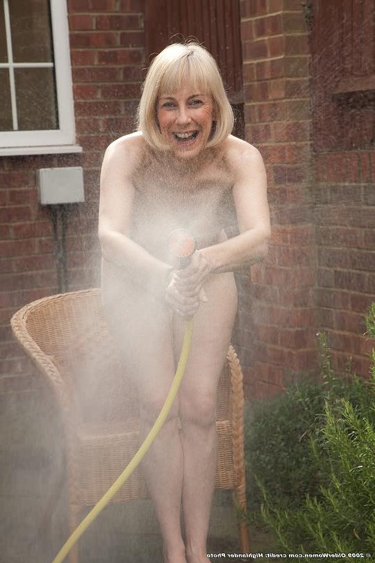 16P Athletic sixtyish gal outdoors in gardenhose spray